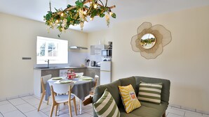 Une cuisine moderne avec un coin repas, un canapé vert agrémenté de coussins à rayures et une décoration murale originale.