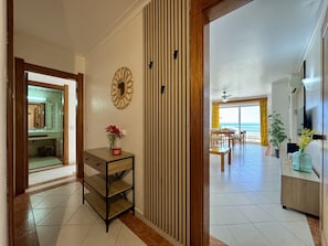A hallway leading to a dining area with a view of the ocean, a wooden cabinet with a vase of flowers, and a mirror on the wall. - ALBUFEIRA AMAZING VIEW 2 WITH POOL by HOMING (Albufeira)