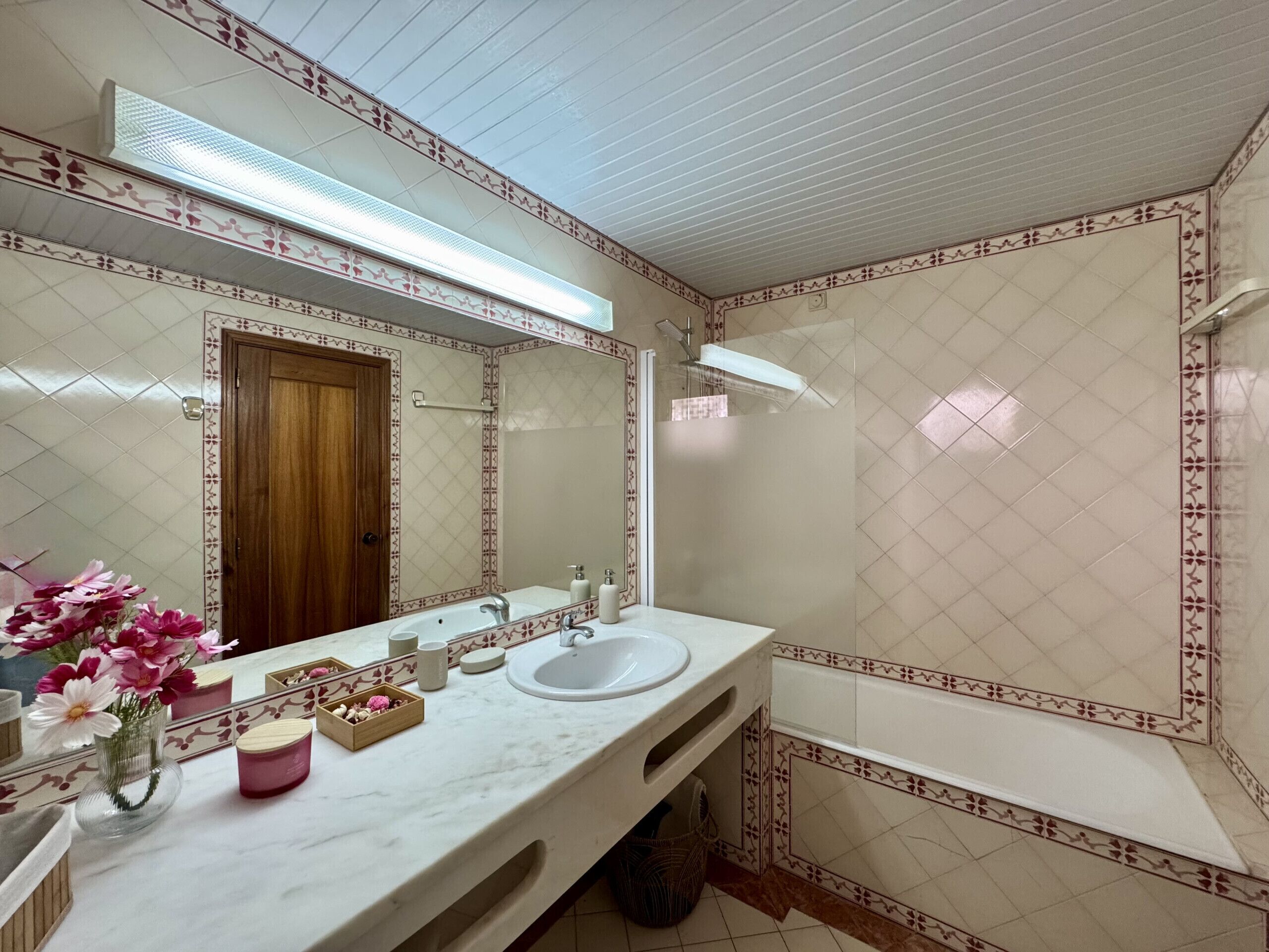 Un baño con lavamanos doble, un espejo grande, una puerta de madera y una zona de ducha.