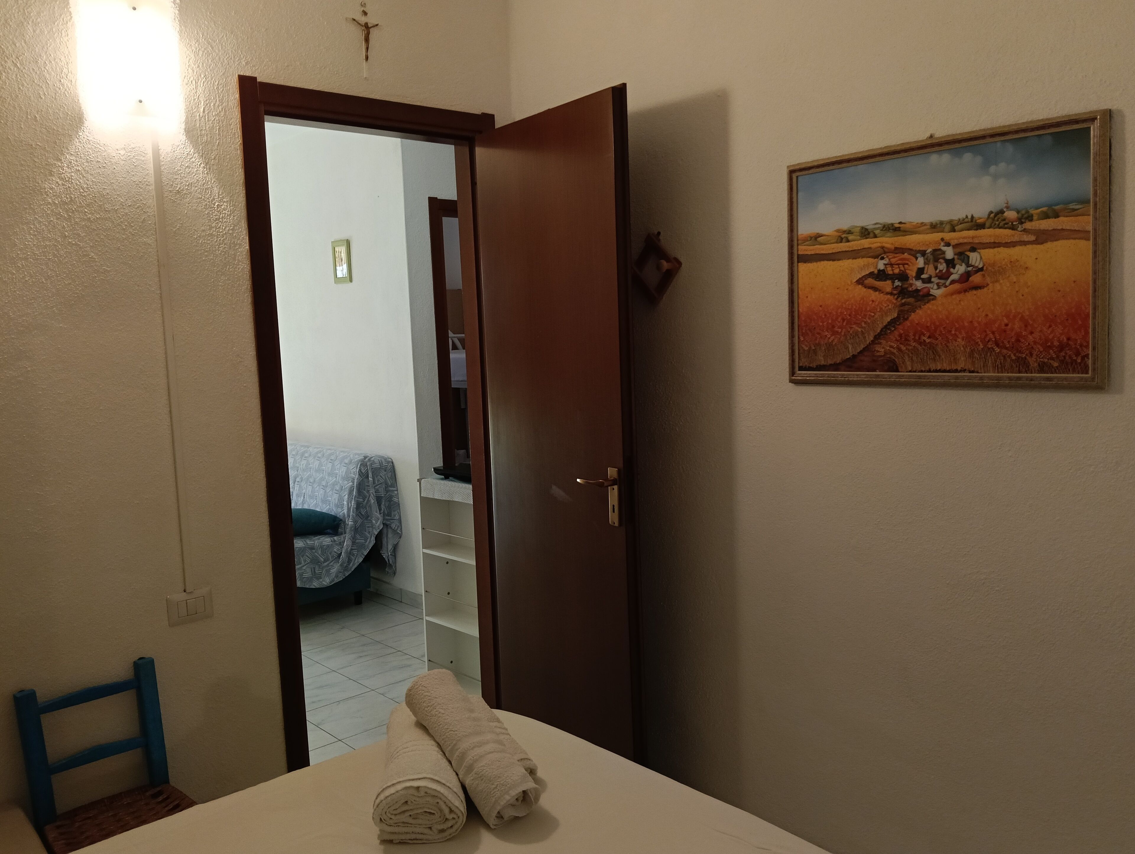 Une pièce comprenant un lit, une chaise, un tableau et une porte donnant sur une autre pièce.