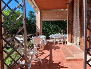 Area patio esterna con tavolo apparecchiato per mangiare, sedie e zona salotto coperta.