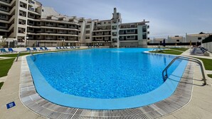 Ein Swimmingpool, umgeben von einer Liegefläche mit Liegestühlen und einem Pooldeck, mit einem mehrstöckigen Gebäude im Hintergrund.