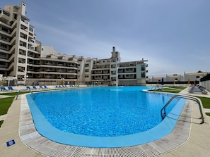 A swimming pool surrounded by a poolside area with lounge chairs, a pool deck, and a multi-story building in the background. - ALBUFEIRA SKYLIGHT 3 WITH POOL by HOMING (Albufeira)