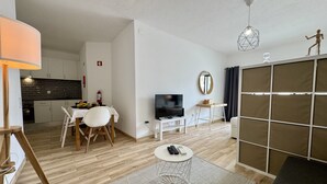 Ein modernes Wohnzimmer mit Fernseher, einem Esstisch und einer Küche im Hintergrund.