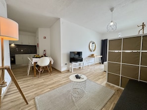 A modern living room with a TV, a dining table, and a kitchen in the background. - ALBUFEIRA SKYLIGHT 3 WITH POOL by HOMING (Albufeira)