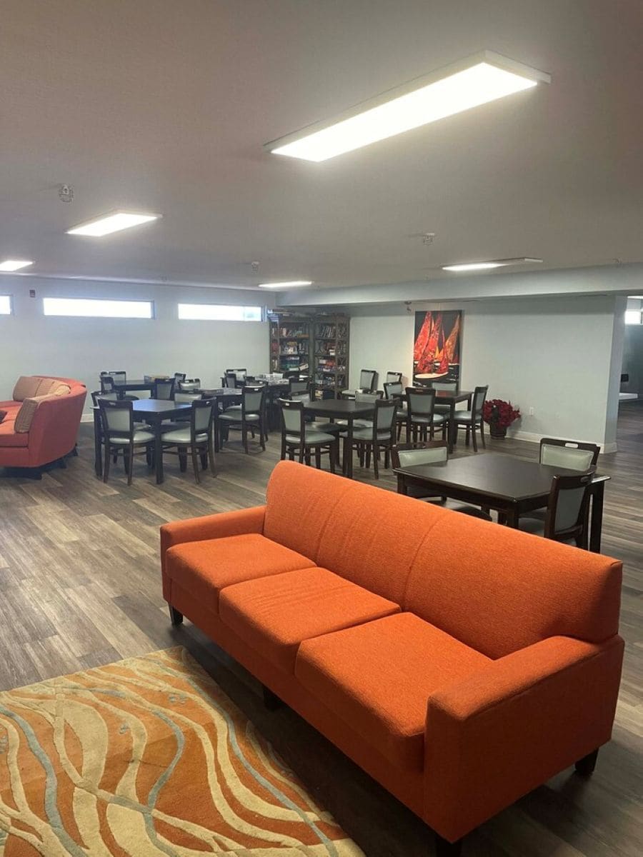 A spacious room with a large orange sofa, multiple dining tables, and chairs.