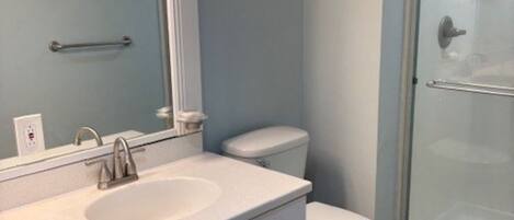 Un baño con lavabo, espejo, inodoro y cabina de ducha de vidrio.