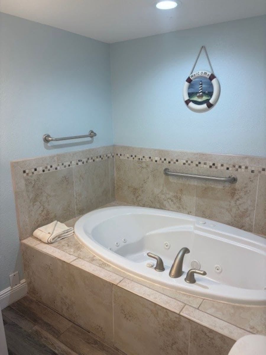 A bathroom with a bathtub, grab bars, and a 'Welcome' sign.