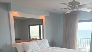 Een hotelkamer met een groot bed, een plafondventilator, een nachtkastje en uitzicht op zee.