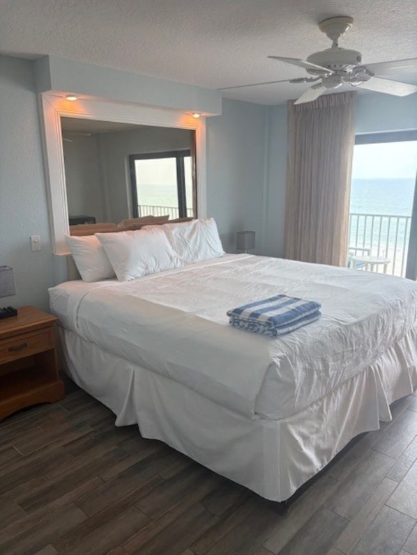 A hotel room with a large bed, a ceiling fan, a nightstand, and a view of the sea.