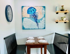 Un comedor con una mesa dispuesta para cuatro, un reloj de pared y un cuadro de una medusa.