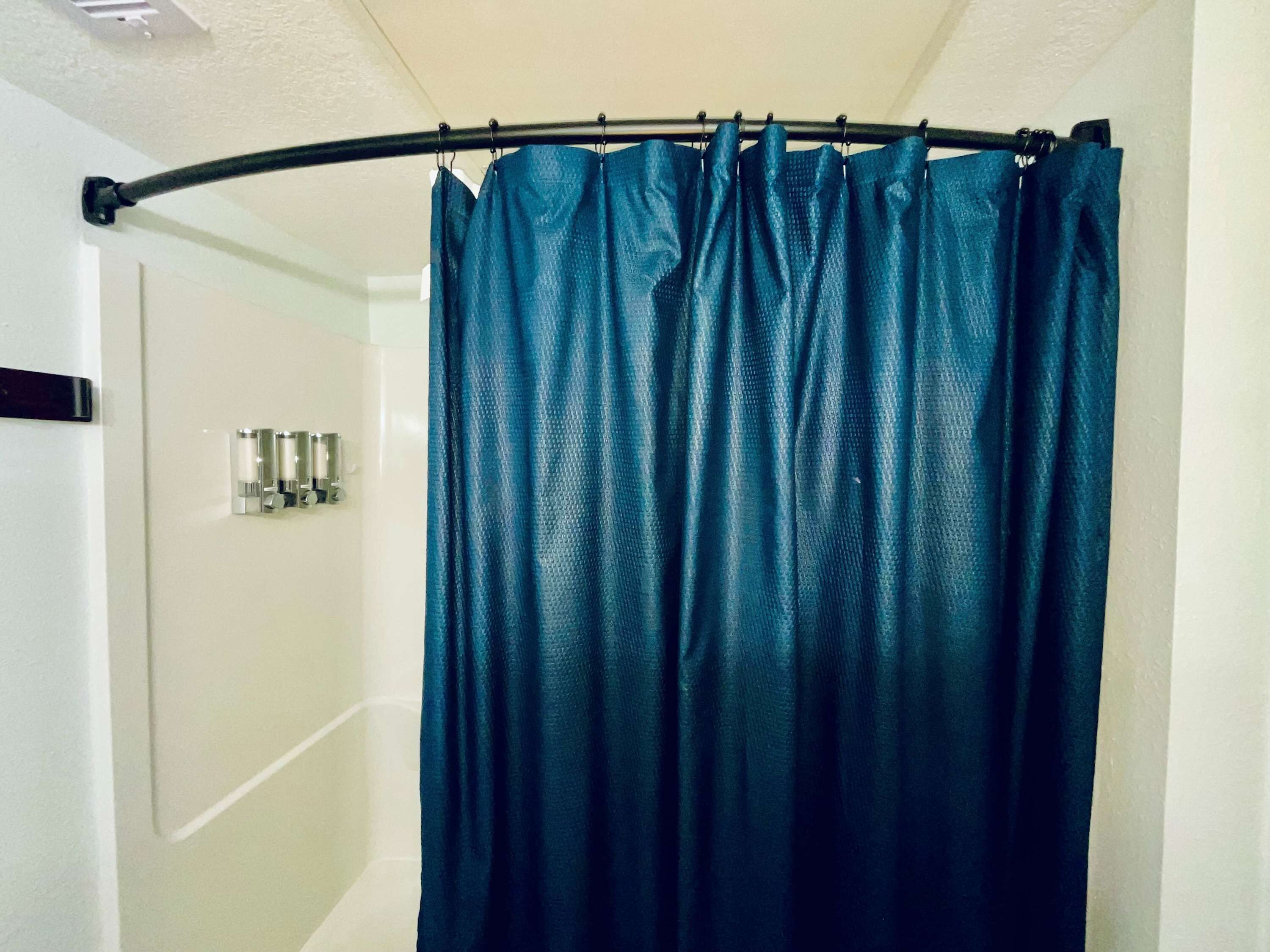 A bathroom with a shower curtain, a hand dryer, and a wall-mounted light fixture.