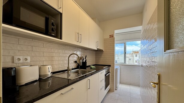 Cozinha moderna com armários brancos, bancada preta e janela com vista para a cidade.