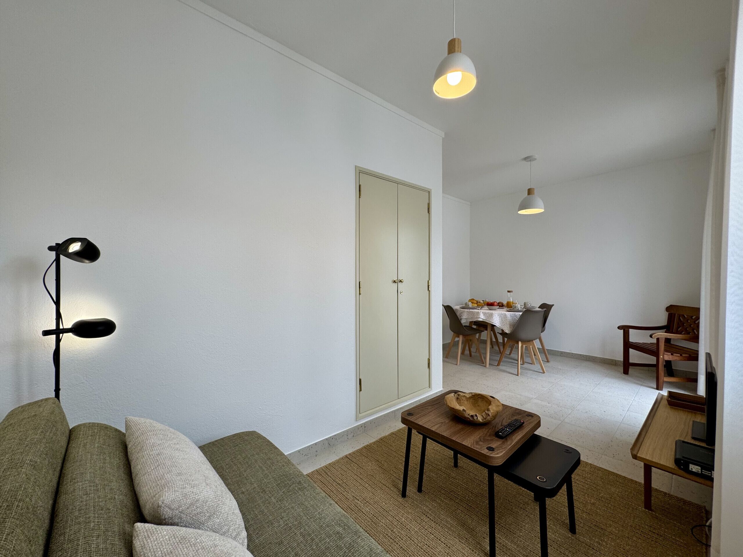 A living room with a sofa, a coffee table, a dining area with a table and chairs, and two pendant lights.