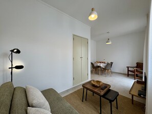 Ein Wohnzimmer mit einer Couch, einem Couchtisch, einem Essbereich mit Tisch und Stühlen sowie zwei Pendelleuchten.