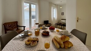 Uma sala de jantar com uma mesa posta para o café da manhã, um sofá e uma televisão ao fundo.