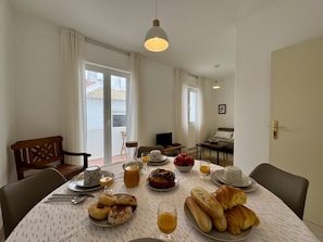 Ein Essbereich mit einem für das Frühstück gedeckten Tisch, einer Couch und einem Fernseher im Hintergrund.