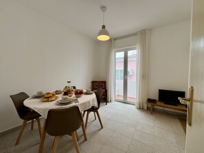 Ein Essbereich mit einem für vier Personen gedeckten Tisch, Stühlen, einem Fernseher auf einem Schrank und einer Glasschiebetür zu einem Außenbereich.
