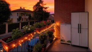 En balkon med lyskæder, plantekasser og et hvidt skab.
