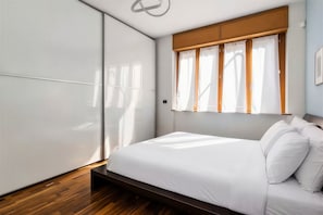 Ein modernes Schlafzimmer mit Bett, Holzboden und einem Fenster mit Vorhängen.