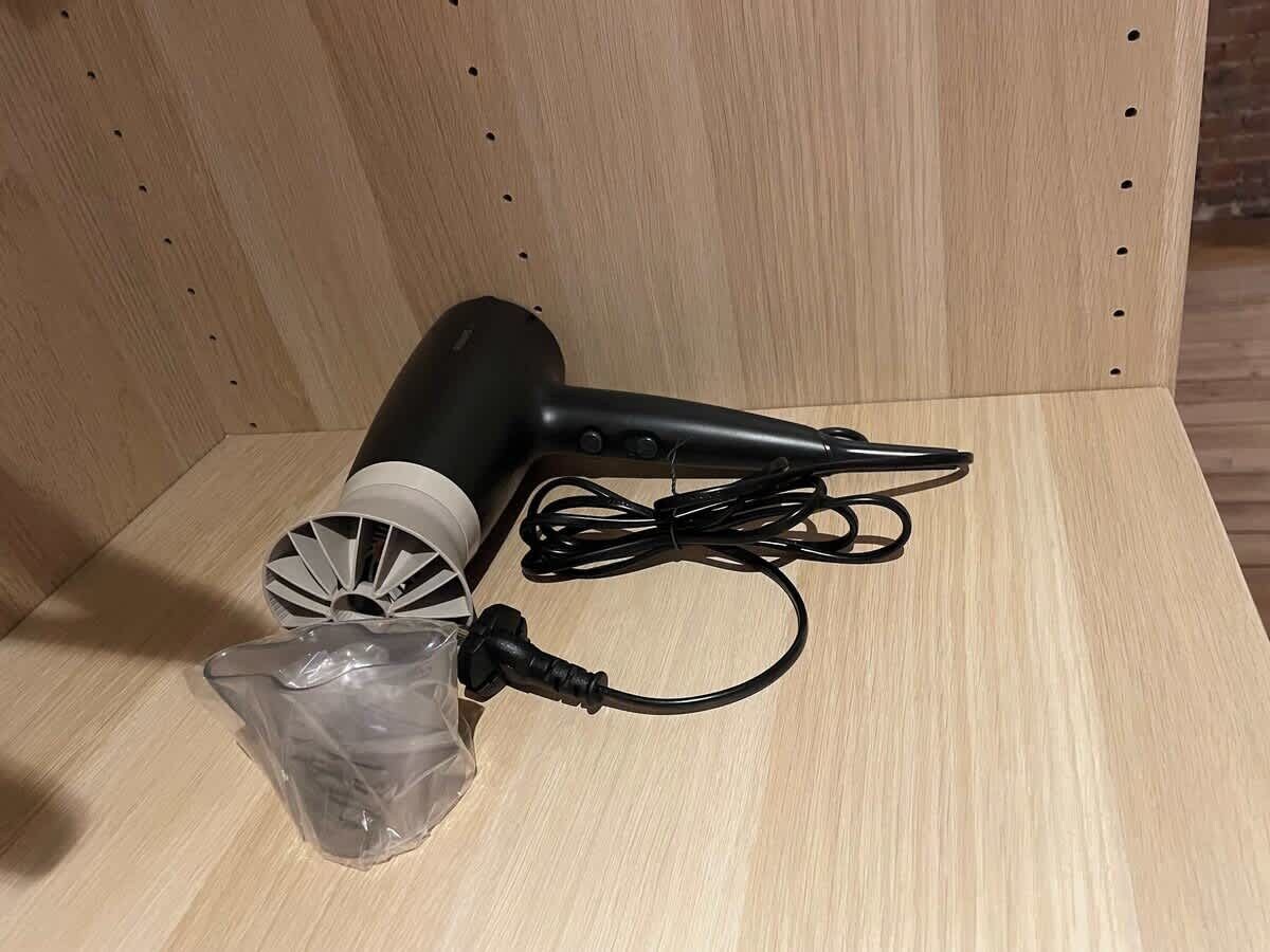 Un assecador i el seu cable d'alimentació sobre una superfície de fusta.