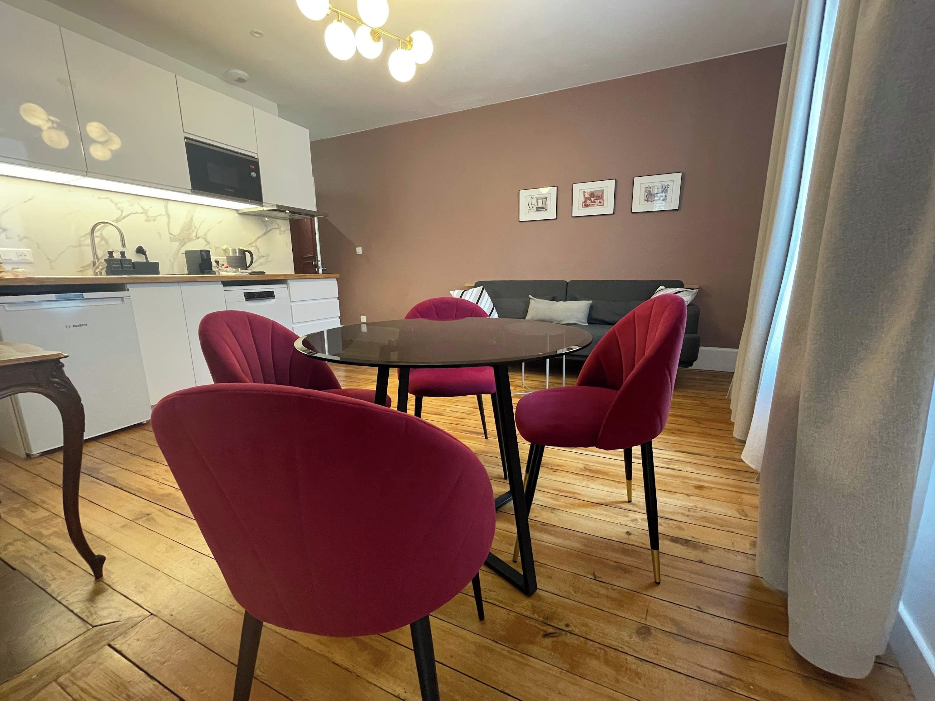 Una cocina moderna con armarios blancos, un lavavajillas Bosch y un comedor con una mesa redonda y sillas rojas.