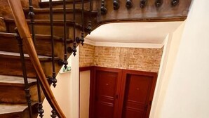 Uma escada de madeira com design curvo, que dá acesso a um quarto com parede de tijolos e portas de madeira.