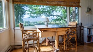 Ein Essbereich mit Tisch und Stühlen, einer Lampe und Blick auf Bäume durch große Fenster.