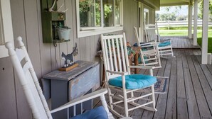 Eine Veranda mit weißen Schaukelstühlen und einem kleinen Tisch mit einer Katzenfigur.