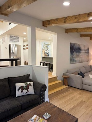 A modern living room with a dark grey sofa, a wooden coffee table, and a grey sofa. There is a staircase leading to an upper level. - Lakefront Escape in Hot Springs 2BR/2BA, Hot Tub, Fireplace & Boat Slips (Hot Springs National Park)