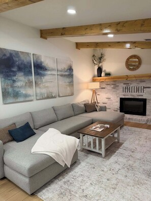 A living room with a grey sofa, a coffee table, a fireplace, and abstract wall art.