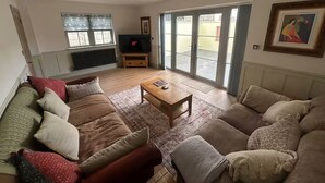 Een woonkamer met een zithoek, een salontafel, een televisie en een schuifdeur naar buiten.