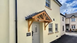 Een gebouw met een lichtgekleurde gevel, een houten veranda en een deur met de tekst 'Sage Cottage 15A'.