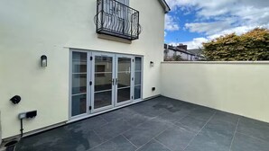 Een gebouw met een balkon, een schuifpui en een betegeld terras.