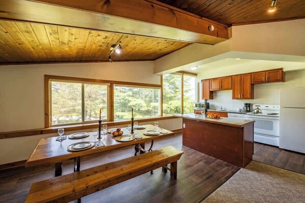 A modern kitchen with wooden cabinetry, a central island, and a dining area with a wooden table and benches.
