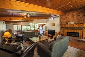 A cozy living room with a fireplace, a television, and a dining area with a kitchen in the background.
