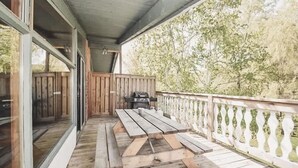 A covered outdoor area with a wooden deck, a picnic table, and a grill.