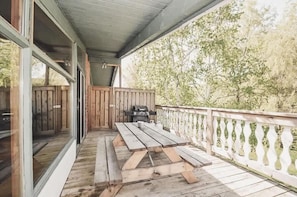 Un espacio al aire libre techado con terraza de madera, una mesa de picnic y una parrilla.