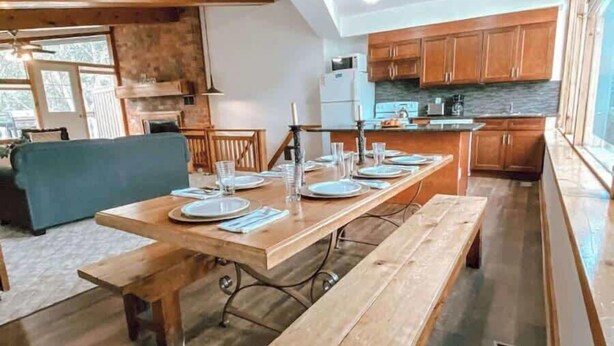 A dining area with wooden tables and benches, a kitchen with wooden cabinets, and a view of the outdoors.