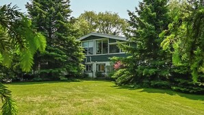 A two-story house with a green roof, surrounded by lush greenery and a well-maintained lawn.