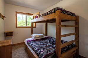 A bunk bed room with a window, a small wooden desk, and a plain wall.