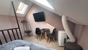 A small, modern room with a bed, a TV mounted on the wall, a heater, and a window.