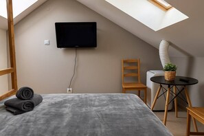 Une chambre à coucher avec un lit, un téléviseur fixé au mur, une petite table avec une plante et une chaise.