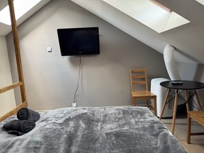 Une pièce comprenant un lit, un téléviseur fixé au mur, une chaise, une petite table et un radiateur.