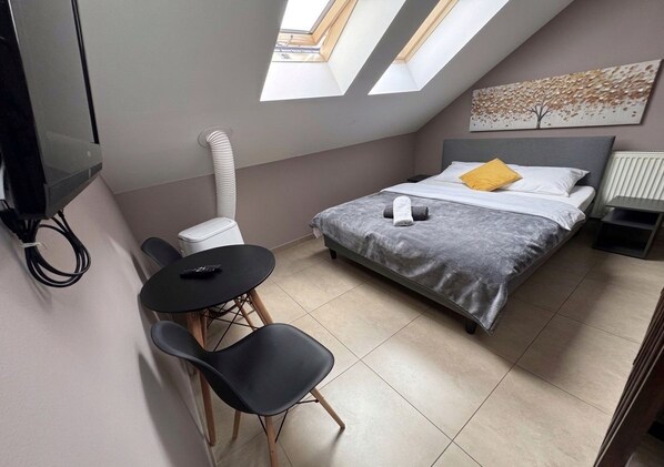 Une chambre à coucher comprenant un lit, un bureau, deux chaises, un téléviseur et une fenêtre de toit.
