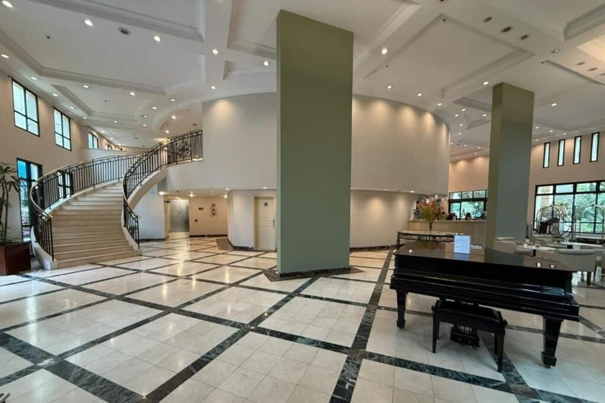 Um hall amplo com um piano de cauda, piso de mármore e escadaria para os andares superiores.