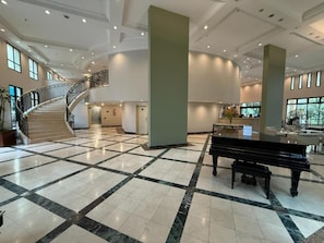A spacious lobby with a grand piano, a marble floor, and a staircase leading to upper levels. - Lume Pinheiros Flat (São Paulo)
