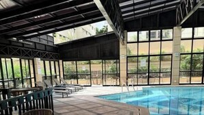 En indendørs swimmingpool med flisegulv, omgivet af liggestole og et overdækket siddeområde.