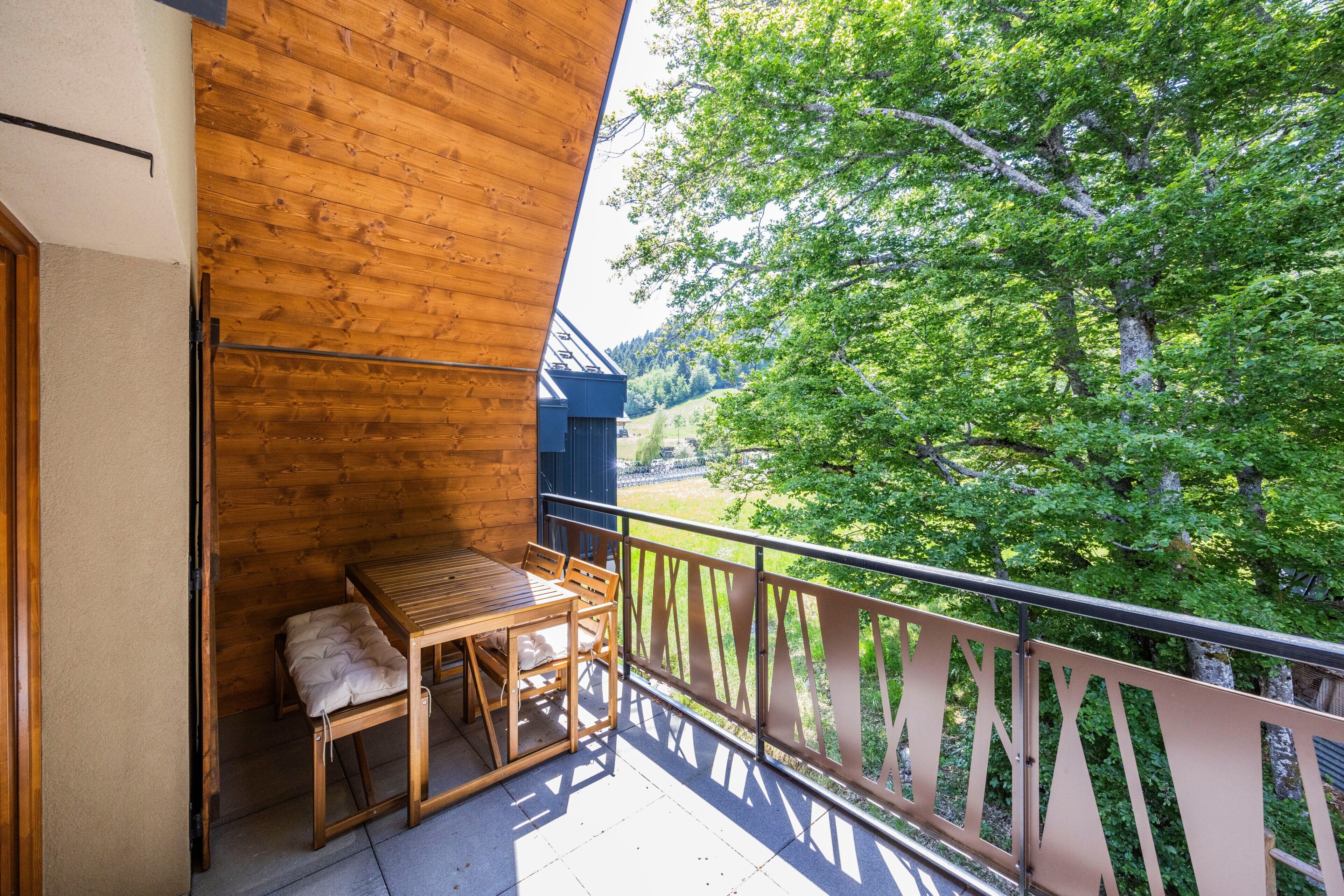 A wooden balcony with a table and chairs, overlooking a forested area.