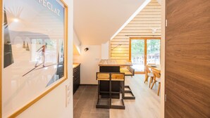 A modern kitchen with wooden cabinets, a dining area with a table and chairs, and a large framed picture on the wall. - “L’aubier des Bauges” Apartment: Mountain View, Private Terrace, Wi-Fi (Les Déserts)